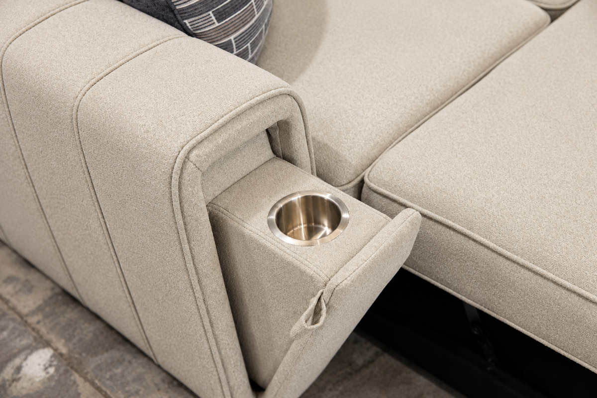 Close-up of a light beige upholstered reclining sofa with a side compartment opening to reveal a stainless steel cup holder.