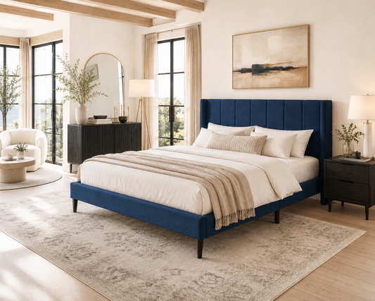 A modern upholstered bed frame in deep blue, styled in a bright, contemporary bedroom with white bedding, beige throw blanket, dark wood nightstands, and a large patterned area rug.